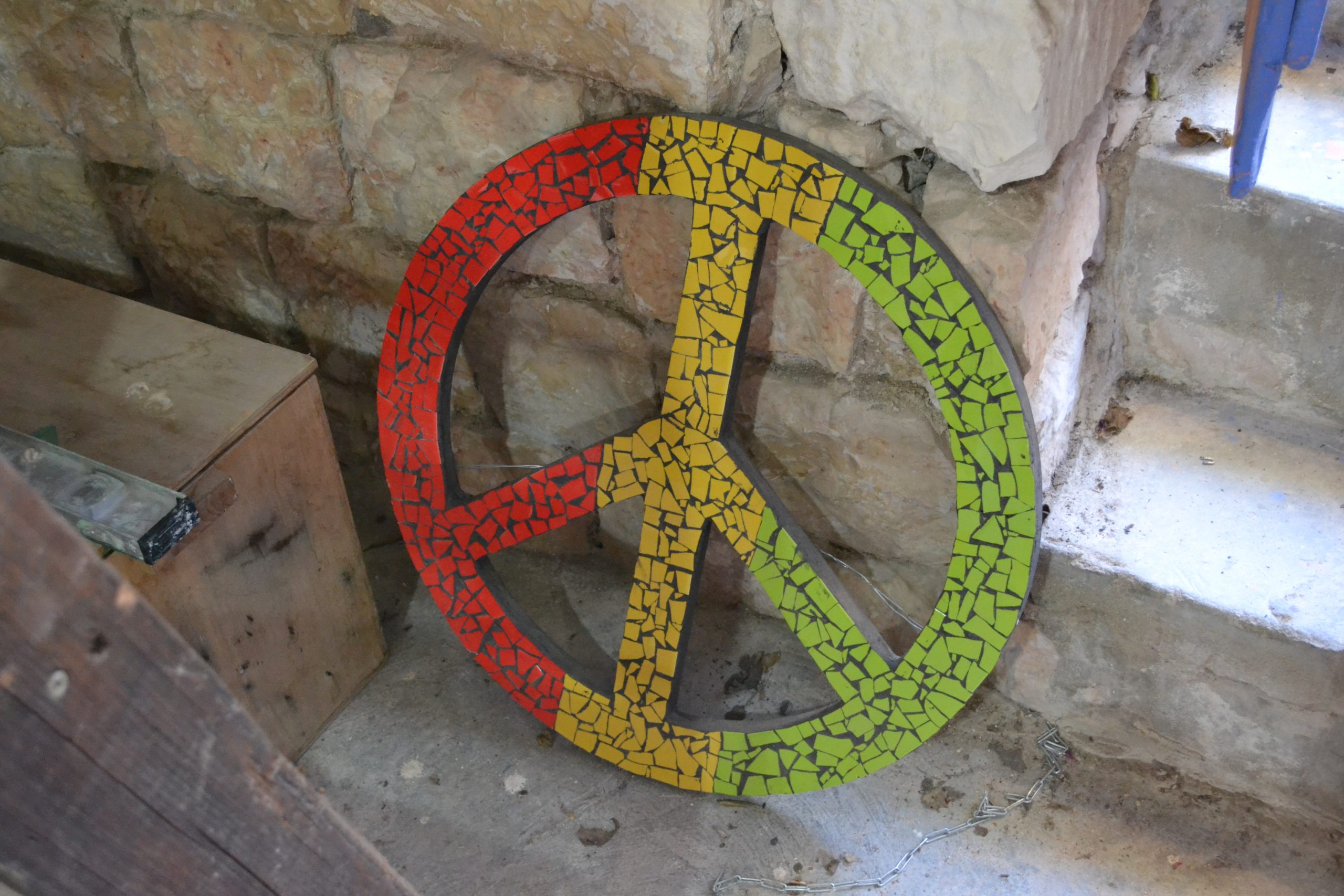 Ein Peace-Zeichen aus Mosaiksteinen, angelehnt an eine Wand. 